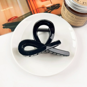 Close-up of a glossy black hair claw clip with a twisted design on a white ceramic plate