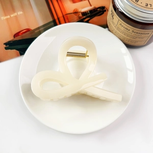 Detail of cream bow hair claw clip with gold metal spring on a decorative tray