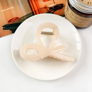 Chic beige bow hair claw clip displayed on a ceramic tray with a scented candle