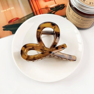Detail view of a glossy amber tortoiseshell hair claw clip on a white ceramic plate