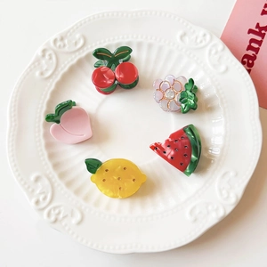 Detailed view of five colorful fruit-shaped hair clips including cherry and lemon designs