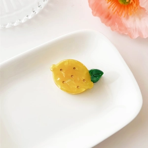 Detailed view of a cute yellow lemon hair claw clip with green leaf on white ceramic tray