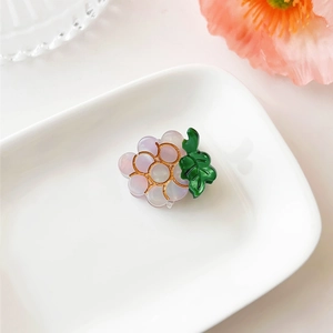 Detail shot of a purple grape acetate hair claw clip with golden trim on a ceramic plate