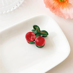 Close-up of a small cherry hair claw clip with glossy red spheres and green leaves