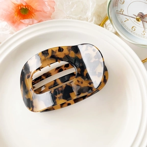 Detail of elegant amber tortoiseshell hair claw clip with hollow oval design on a plate