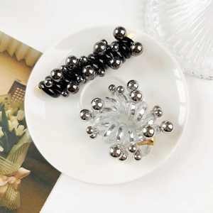 Detail of spiral hair ties in black and clear with shiny silver metallic beads in a tray