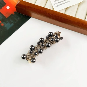 Detail of beaded hair tie with dark grey spheres and translucent base on a wooden tray