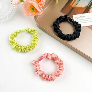 Close-up of three satin scrunchies in black, green, and pink with plastic buckles