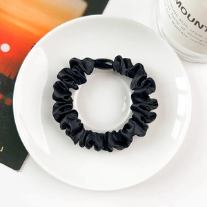 Detailed macro view of black satin scrunchie with an elegant oval buckle on white ceramic dish