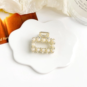 Dettaglio di una mini molletta per capelli dorata con perle su un piatto di porcellana