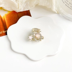 Dettaglio di mini molletta dorata con perla rosa e stella su un vassoio floreale