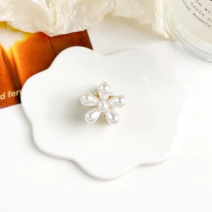 Dettaglio di elegante molletta per capelli con perle e petali dorati su un piatto di ceramica