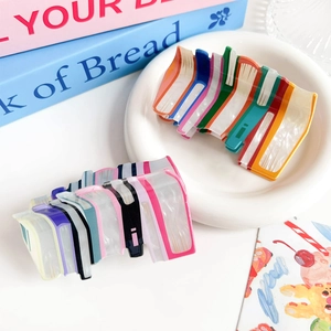 Detail showing two colorful acrylic book-shaped hair claws in vibrant and Morandi tones