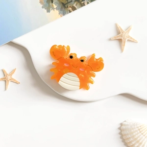 Gros plan sur une pince à cheveux crabe orange en acétate sur un support blanc ondulé