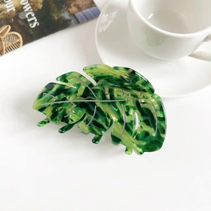 Détail d'une pince à cheveux en forme de feuille verte en acétate avec un motif marbré élégant
