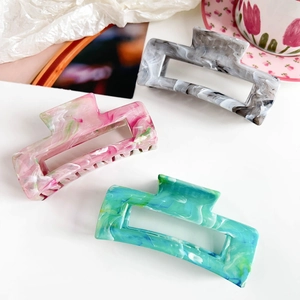 Three large marble pattern rectangular hair claws in pink, grey, and teal acetate