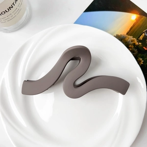 Detail of a large matte brown wavy claw clip on a white ceramic plate for thick hair