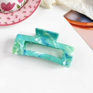 Detail view of large marble hair claw clip with green blue patterns on white background