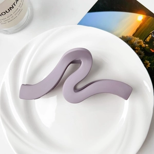 Close-up of matte purple wave claw clip on a white plate with aesthetic background