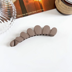Détail de la pince banane évidée marron café mat aux bords ondulés sur un décor de table blanc