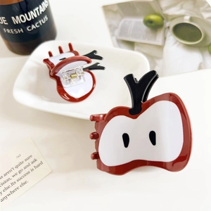 Detail of red apple shaped hair claw clips with strong metal springs on a white tray