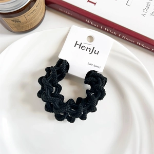 Close-up of black textured elastic hair tie on a white ceramic plate with a cozy background