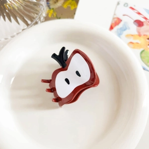 Detail of red apple shaped hair claw clip on a ceramic plate with floral decor