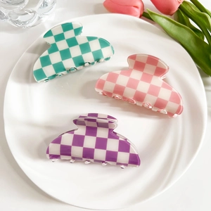 Close-up of checkerboard hair claws in pastel mint, pink, and purple colors on a white plate