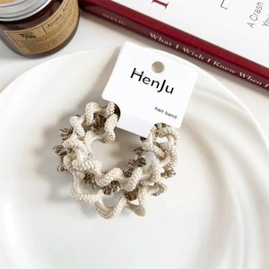 Close-up of beige and coffee spiral woven hair scrunchies on a white porcelain plate