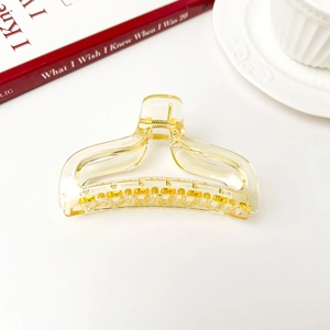 Detailed close-up of amber fishtail hair claw clip with golden teeth on white surface
