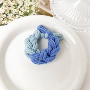Detailed view of blue braided hair tie with thick texture on a white decorative plate