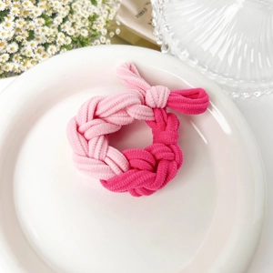 Detail of pink braided elastic hair tie with a small bow on white ceramic plate