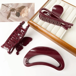 Detailed close-up of three burgundy hair claws on a white surface with luxury tray