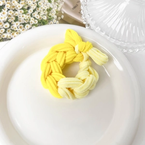 Close-up of yellow braided knit hair tie with bow shape on decorative white plate