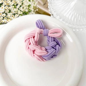 Detail of pink and purple braided hair tie with twisted knot on a white ceramic plate