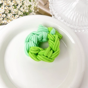 Detail of chunky braided hair tie in green tones on a white decorative ceramic plate