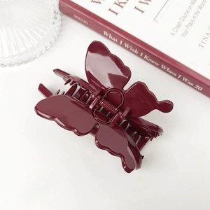 Detailed view of an elegant burgundy butterfly hair claw clip on a minimalist desk