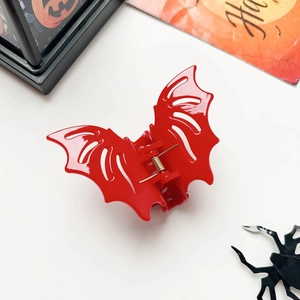 Top view of a glossy red bat hair claw with golden spring and Halloween decor props