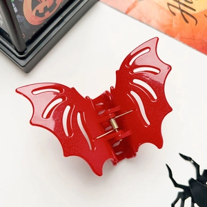 Close-up of a red glittery bat claw clip with Halloween pumpkins and spider decor