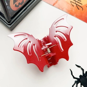 Close-up of red glitter bat hair claw clip with festive Halloween decor on white background