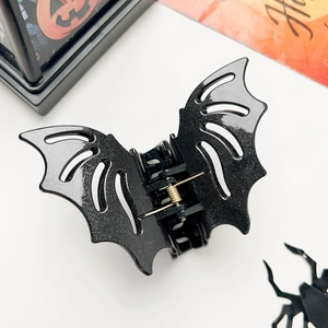 Detail of bat-shaped hair claw clip with black glitter finish and gold metal spring