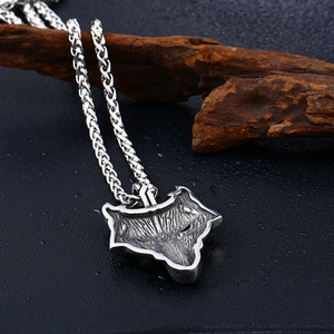 Close-up of a vintage stainless steel wolf head pendant with detailed fur texture on wood