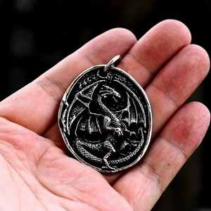 Close-up of vintage stainless steel dragon relief pendant held in hand for size comparison