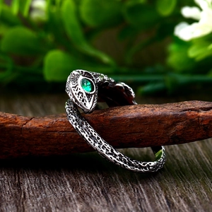 Macro shot of stainless steel lizard ring with green gemstone eyes on wooden branch