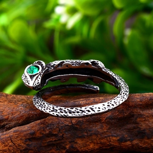 Vintage stainless steel lizard ring with green gemstone on a natural wood surface