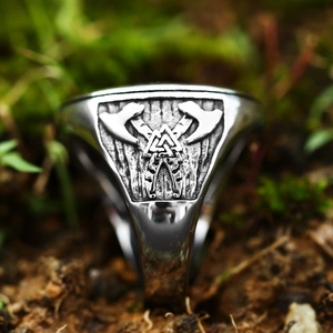 Macro close-up of vintage steel Viking ring with double axes and Valknut on mossy ground