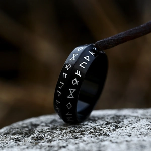 Macro shot of matte black stainless steel Norse Rune ring on a textured grey rock surface