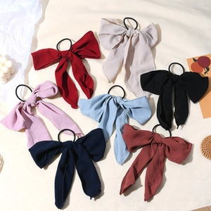 Flat lay of seven colorful chiffon bow hair ties with long ribbons on a beige fabric base
