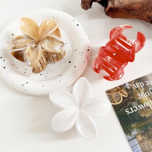 Detailed close-up of marble pattern plumeria hair claws and red acetate clip on decor