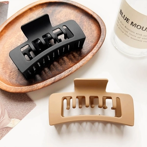 Detail of matte black and khaki hollow rectangular claw clips on a wooden tray